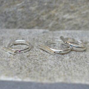Prosty, minimalistyczny i elegancki pierścionek ze srebra z małym rubinem / niebieskim diamentem w obrączce leży na popielatym kamieniu. Element główny ma ustawienie horyzontalne.