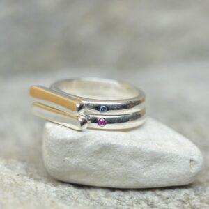 Prosty, minimalistyczny i elegancki pierścionek ze srebra z małym rubinem / niebieskim diamentem w obrączce leży na popielatym kamieniu. Element główny ma ustawienie horyzontalne.