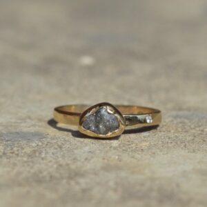 Oryginalny złoty pierścionek o surowym wykończeniu z nieoszlifowanym diamentem i małym brylantem obrączce leży na naturalnym podłożu