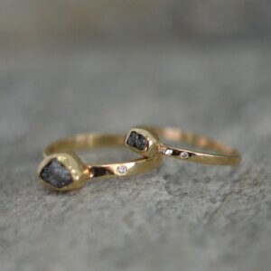 Delikatny złoty pierścionek o surowym wykończeniu z popielatym surowym diamentem i małym różowym brylantem w obrączce leży na szarym kamieniu
