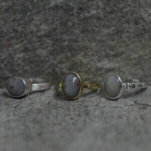 Proste srebrne pierścionki z szarymi szafirami i małymi kamieniami w obrączce leżą na popielatym podłożu. Kamienie główne są owalne